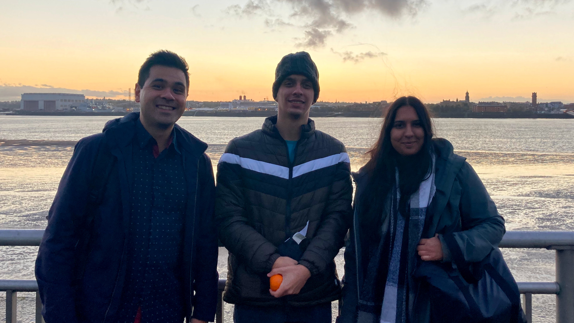 Photo of 3 people smiling with a river and building in the background.